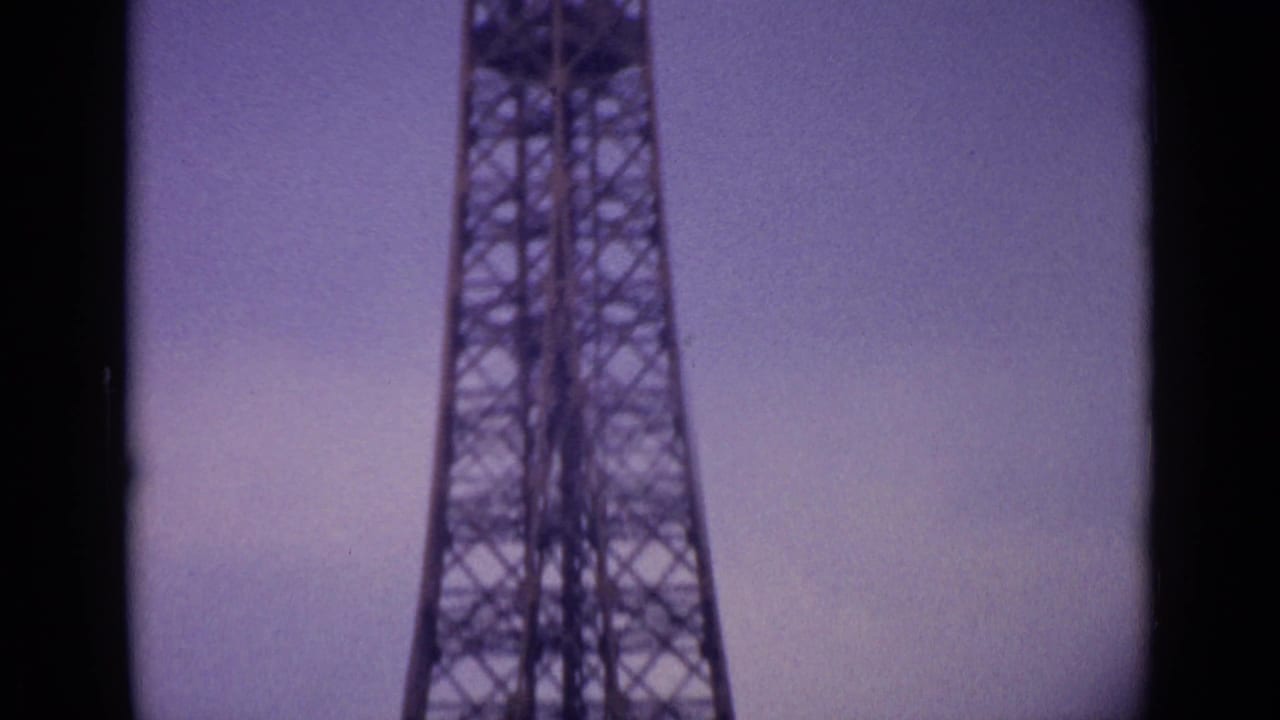 1962 8mm frame of the Eiffel Tower's narrowing lattice section in Paris, tinted purple with grain and soft exposure.