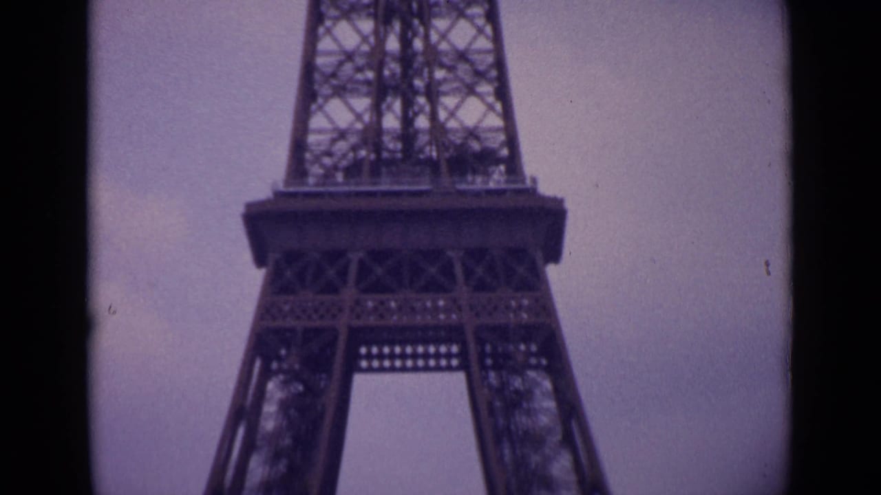 1962 Paris home-movie frame showing the Eiffel Tower's lower platform and legs, with aged 8mm grain and muted color.