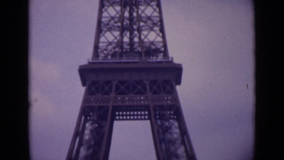 1962 Paris home-movie frame showing the Eiffel Tower's lower platform and legs, with aged 8mm grain and muted color.
