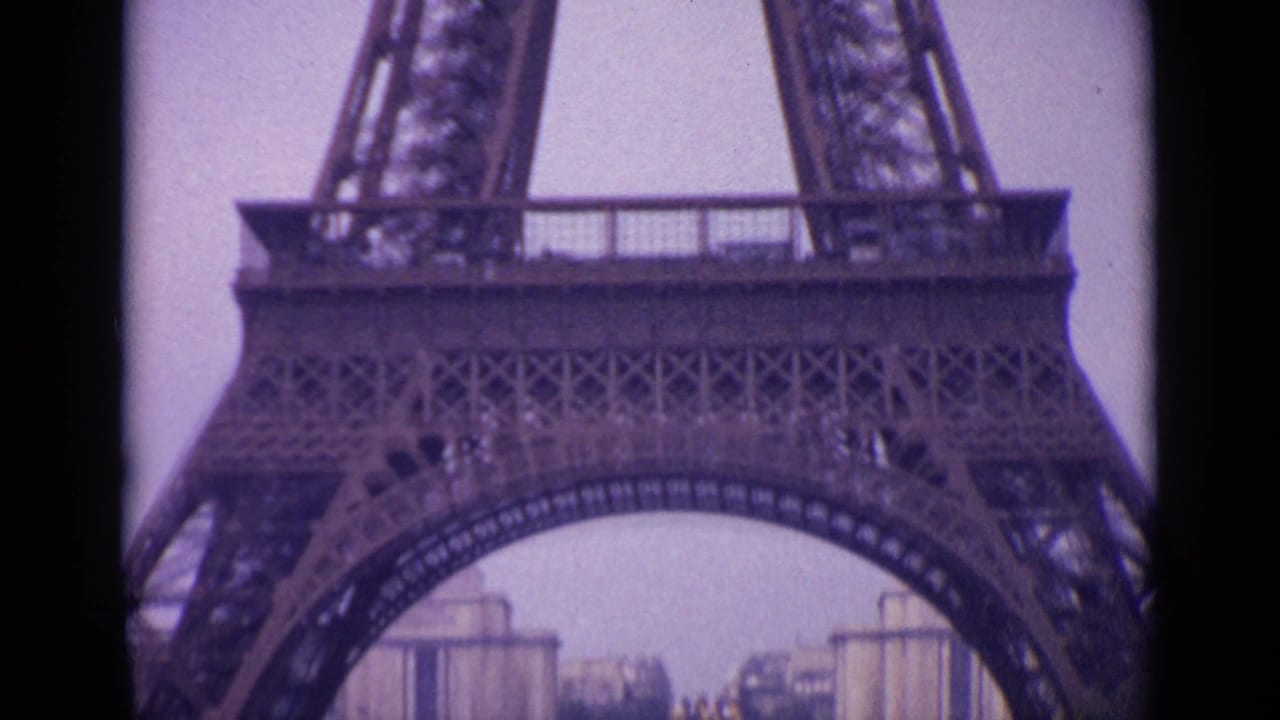 1962 Paris frame showing the Eiffel Tower base arch with distant buildings and tower ironwork seen through soft 8mm color.