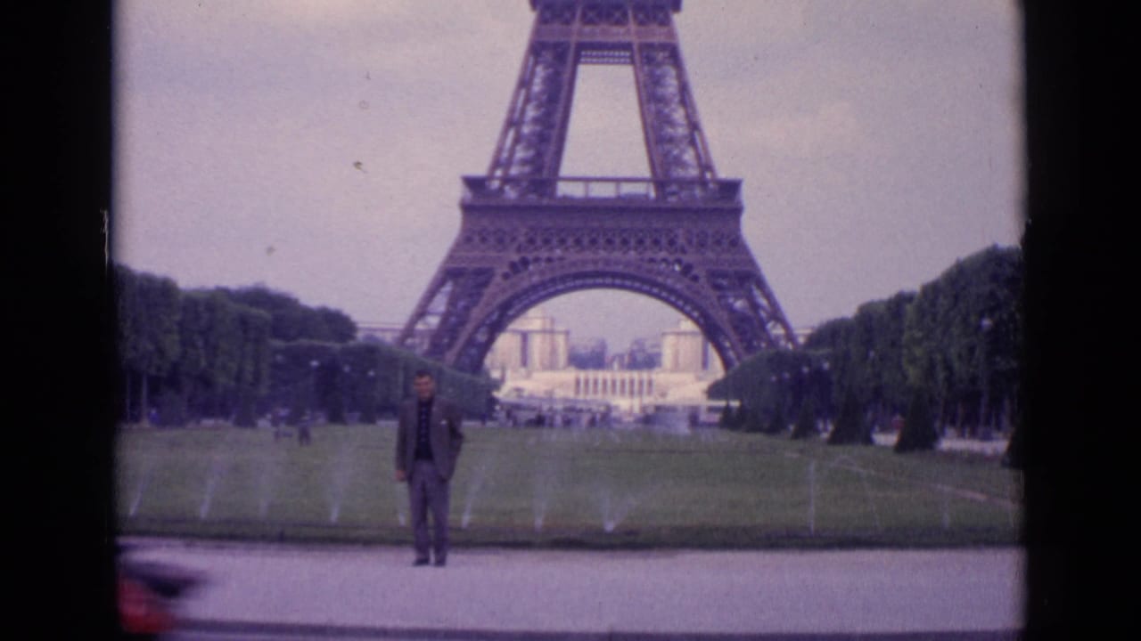 1962 Paris 8mm frame with the Eiffel Tower centered behind a posing man and a blurred person passing near the camera.