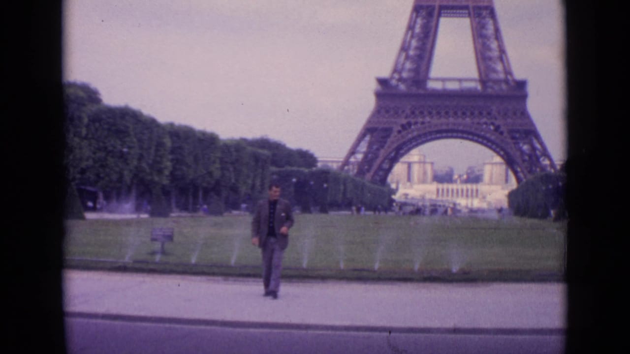 1962 Paris frame showing the suited man walking away from the Eiffel Tower grounds toward the foreground path.