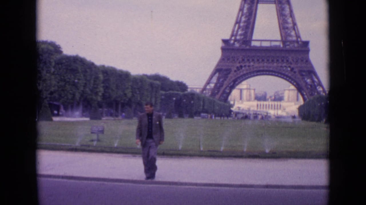 1962 Paris frame with a man in a tweed-style blazer approaching the camera, Eiffel Tower base and fountains visible in the background.