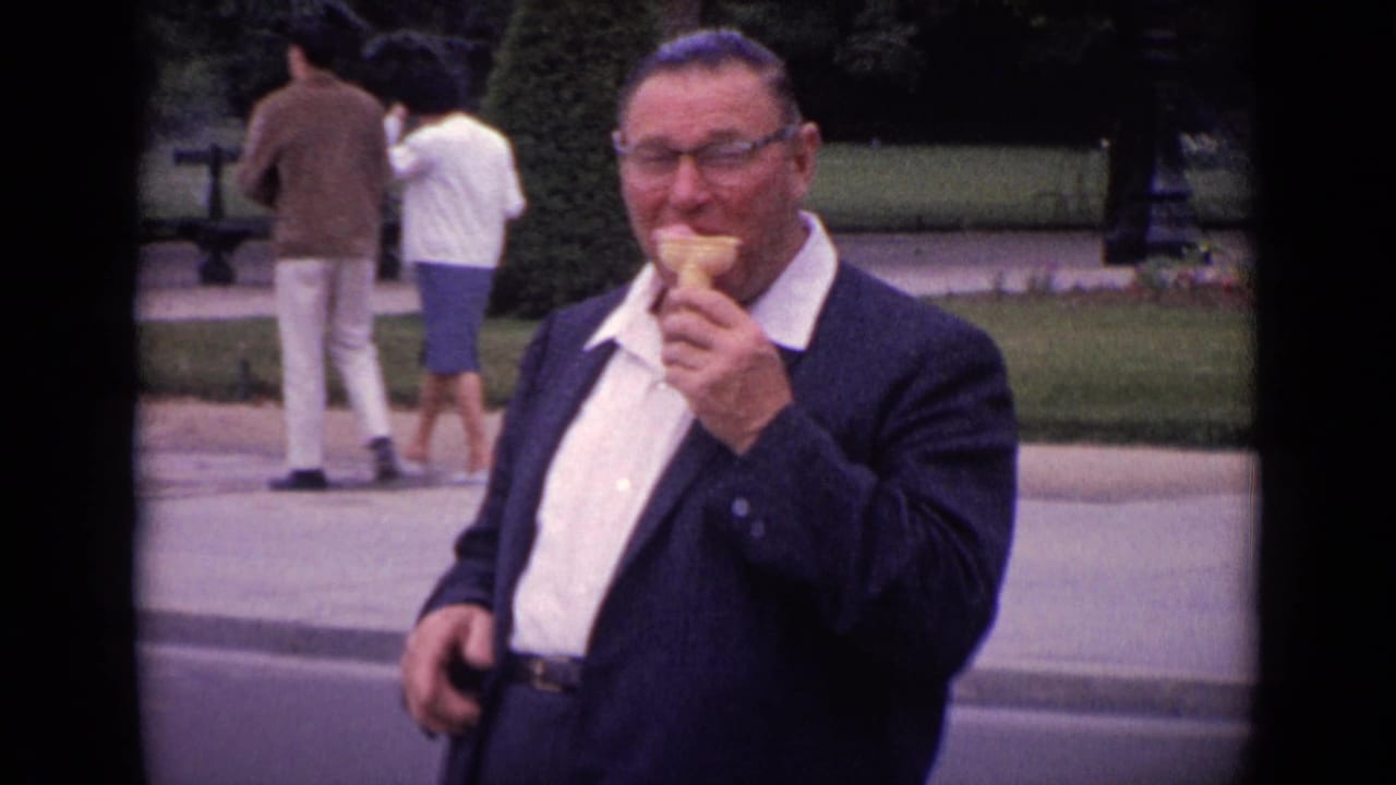 Man in a dark jacket eating an ice cream cone beside a park path.