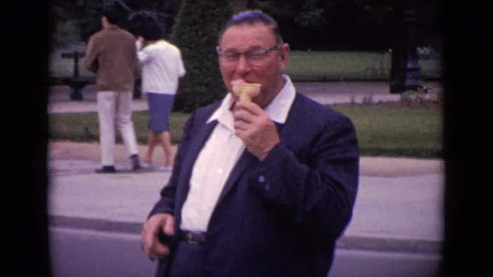 1962 Paris home-movie frame of a man in glasses holding an ice cream cone near a landscaped public path.