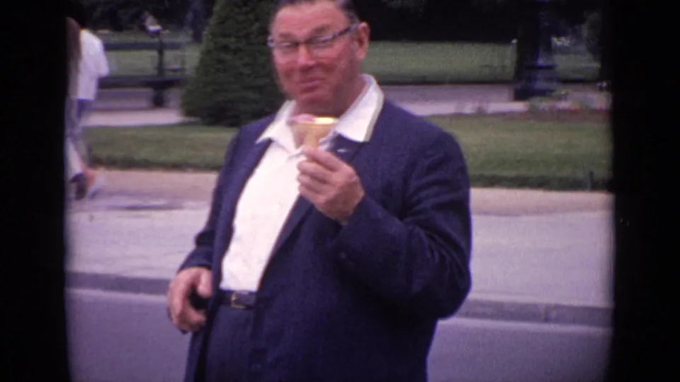 Close 1962 Paris home-movie view of a man in a dark jacket holding an ice cream cone in a public garden setting.