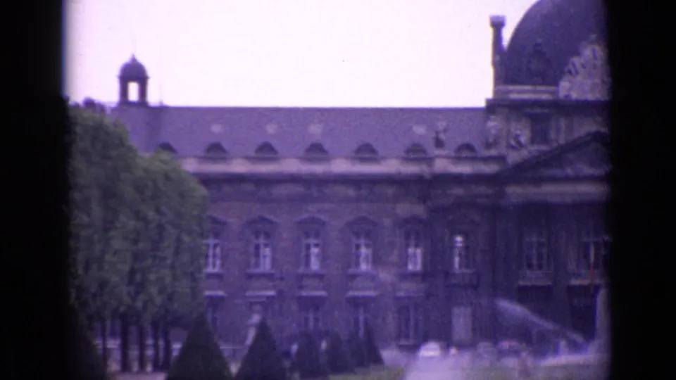 A Paris palace garden view shows a large stone facade with a dome, rows of trees, lawn, and fountain spray in soft 8mm color.