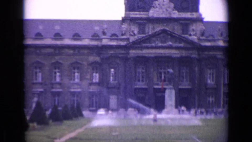 A 1962 Paris garden shot frames the palace front, lawn, fountain spray, trimmed trees, and a central monument in handheld 8mm footage.