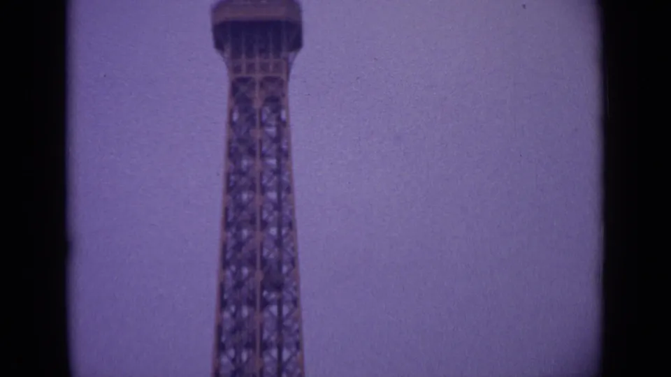 1962 Paris frame showing the Eiffel Tower lattice and upper platform, cropped close against a pale sky.