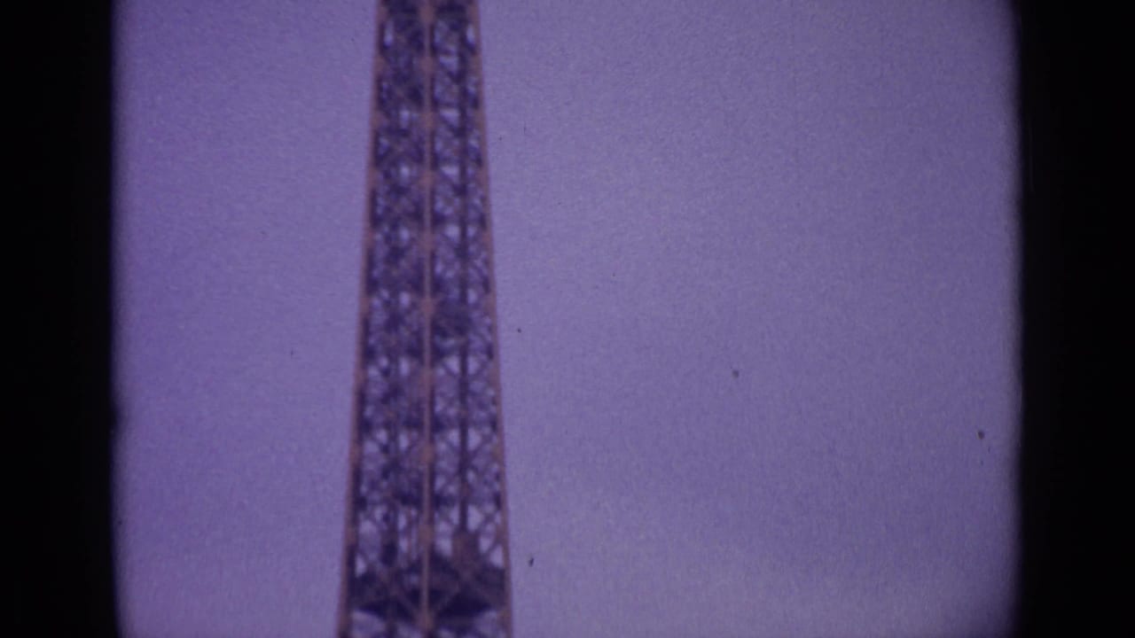 1962 8mm Paris footage showing the Eiffel Tower rising from the lower frame against an overcast, faded purple sky.