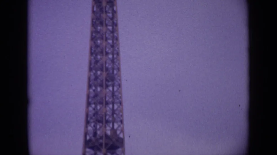 1962 8mm Paris footage showing the Eiffel Tower rising from the lower frame against an overcast, faded purple sky.