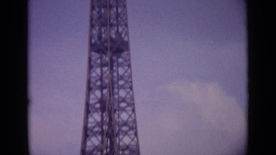 Tight low-angle 8mm view of the Eiffel Tower structure in Paris, with soft focus and faded color from the 1962 home movie.