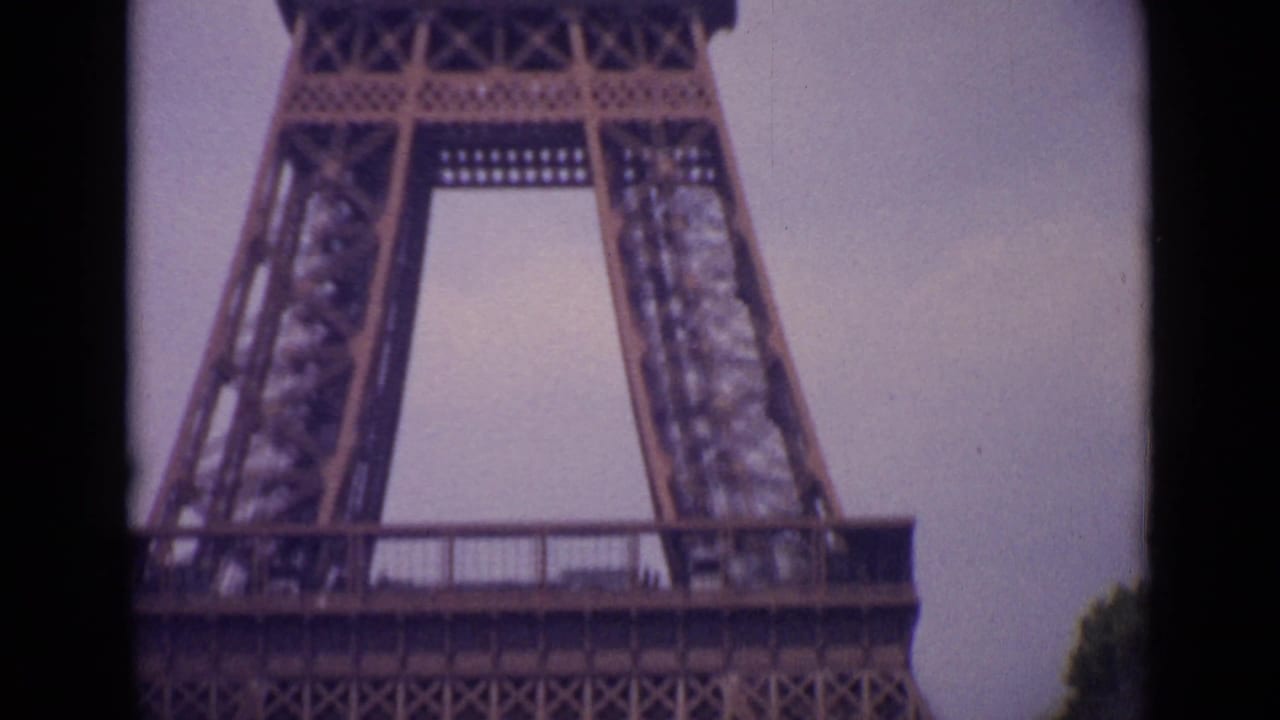 1962 Paris home-movie frame showing a low-angle section of the Eiffel Tower base with soft focus and faded color.
