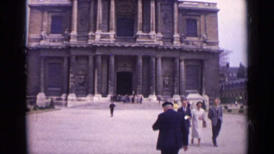 1962 Paris frame with foreground adults walking past a monumental columned facade and open entrance across the plaza.