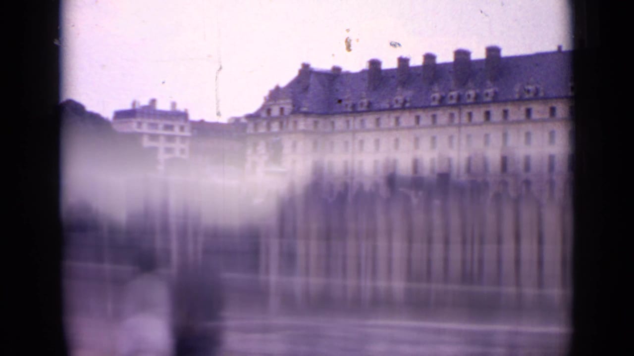 Blurred moving view of a long Paris building behind a stone embankment.