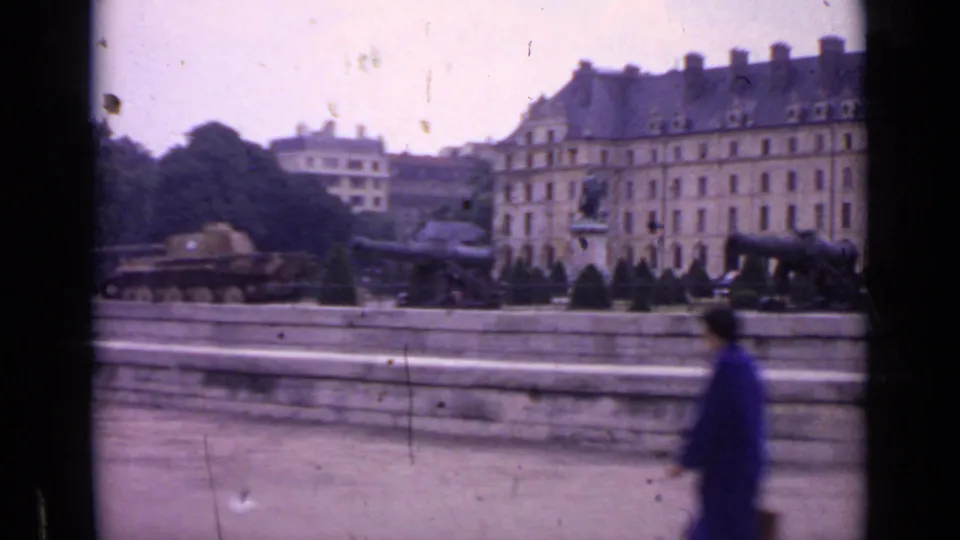 1962 Paris street view showing a formal display area with cannons, a tank, a statue, and a pedestrian passing in a blue coat.
