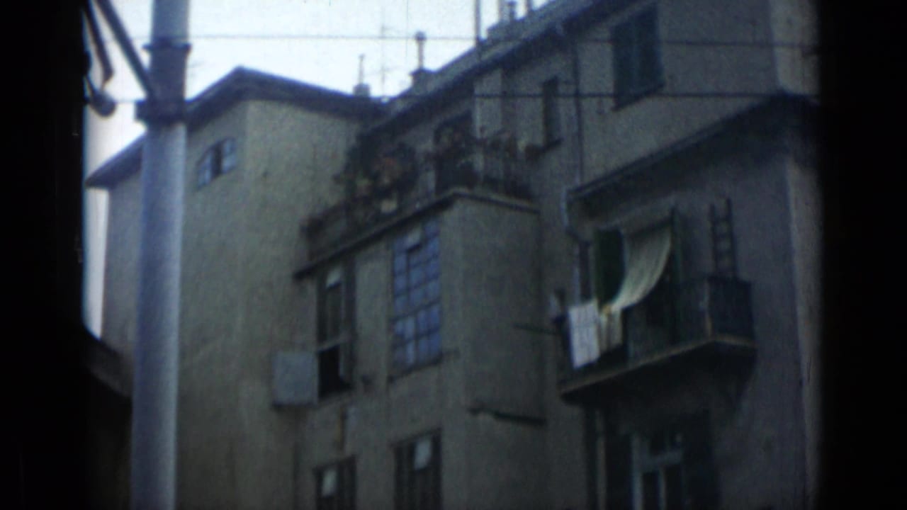 1962 Italy-labeled 8mm frame of a worn apartment facade with balconies, shutters, laundry, and overhead lines.