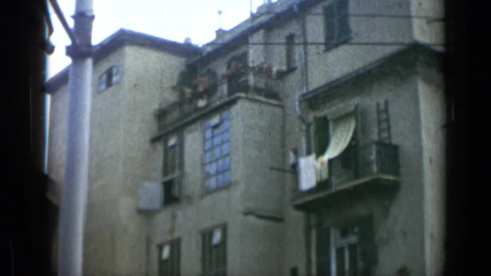 1962 Italy-labeled 8mm frame looking upward at an apartment building with shuttered windows, balconies, and laundry.