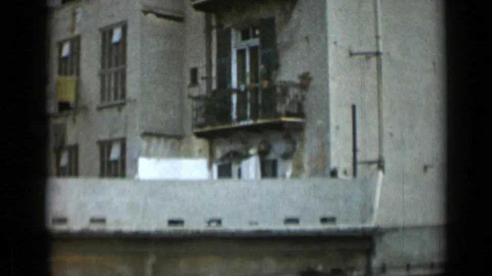 Rome apartment exterior with small balconies, shuttered windows, rooftop edge, and aged wall surfaces.