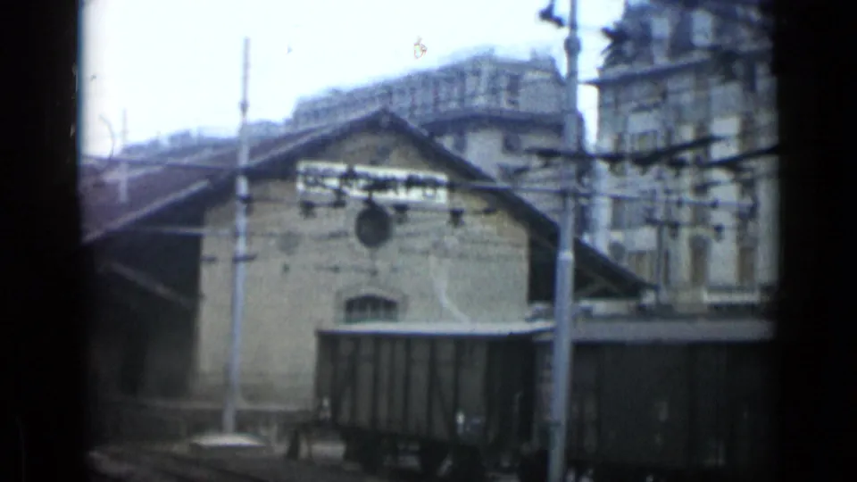 Italian rail yard view with depot roof, GENOVA B sign, freight cars, wires, and blurred 8mm motion.