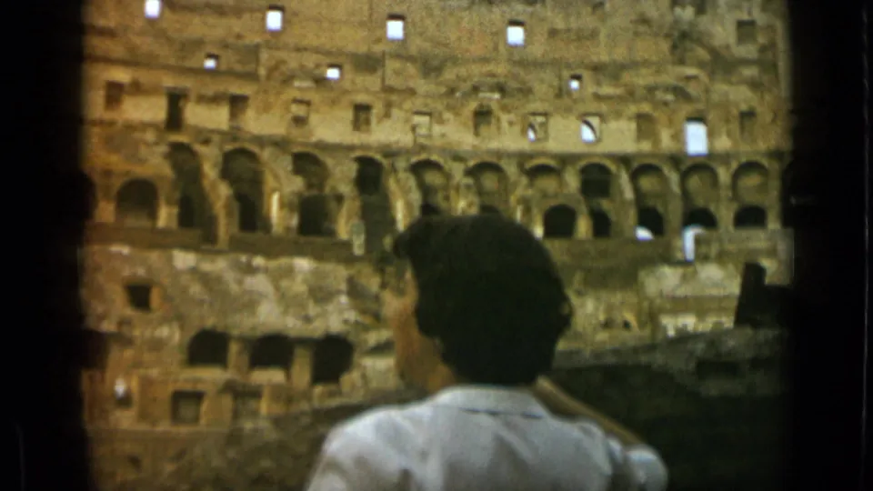 Rome 1962 8mm still with a woman viewed from behind against the Colosseum's layered masonry and arched openings.