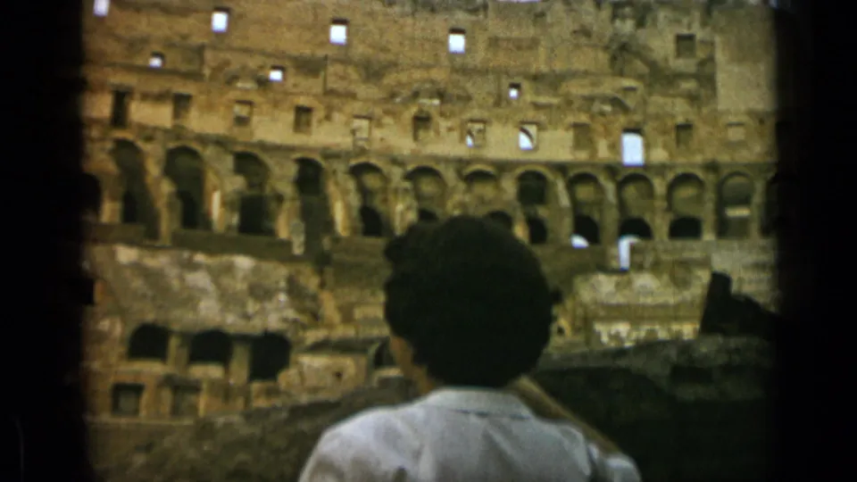 Final 1962 Rome frame of a woman looking at the Colosseum ruins, with faded color and visible 8mm film texture.