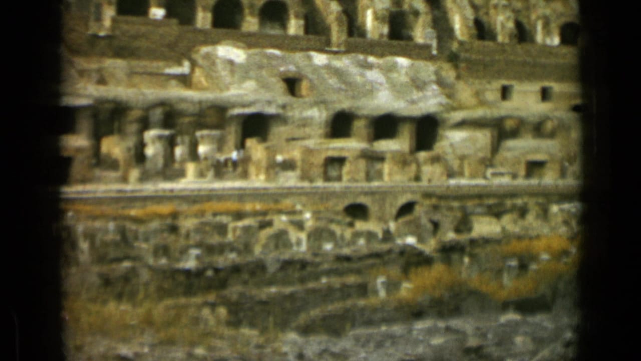 Colosseum interior wall with arches, rough stone, vegetation, and distant people.