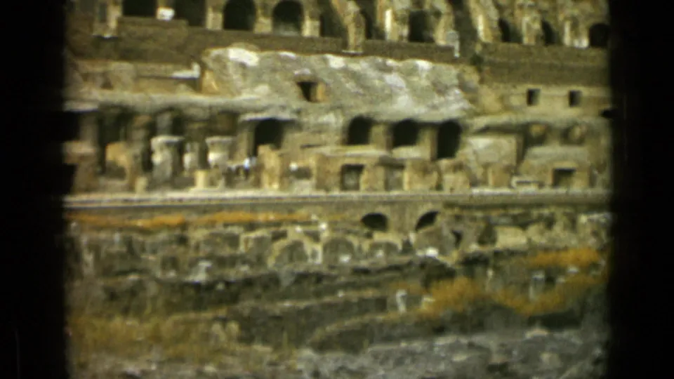 Rome Colosseum interior in 1962, with stacked archways, broken masonry, a lower barrier, overgrowth, and small visitors visible far from camera.