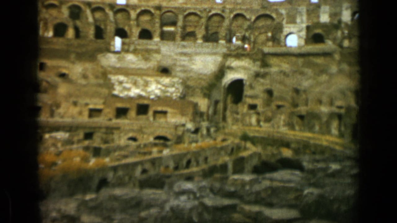 Colosseum ruins with rows of arches, stone openings, and lower arena remains.
