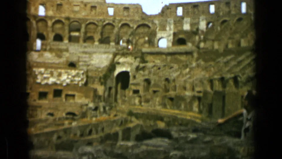 1962 Rome home-movie view of the Colosseum interior, with arched walls, lower ruins, and a small visitor figure at right.