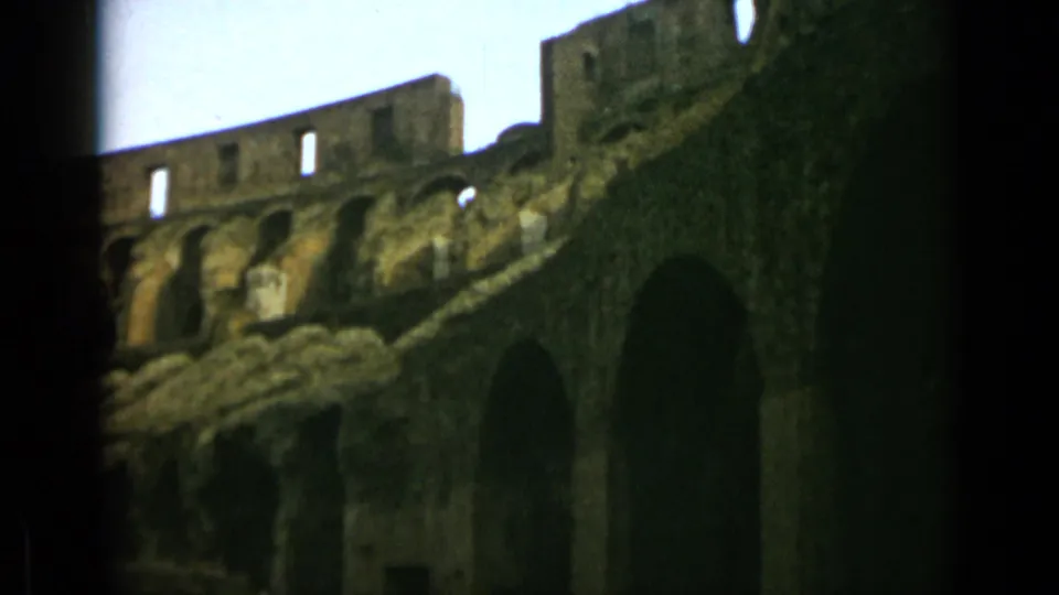 1962 Rome frame showing a shadowed side view of the Colosseum interior with arches, upper wall openings, and pale sky.