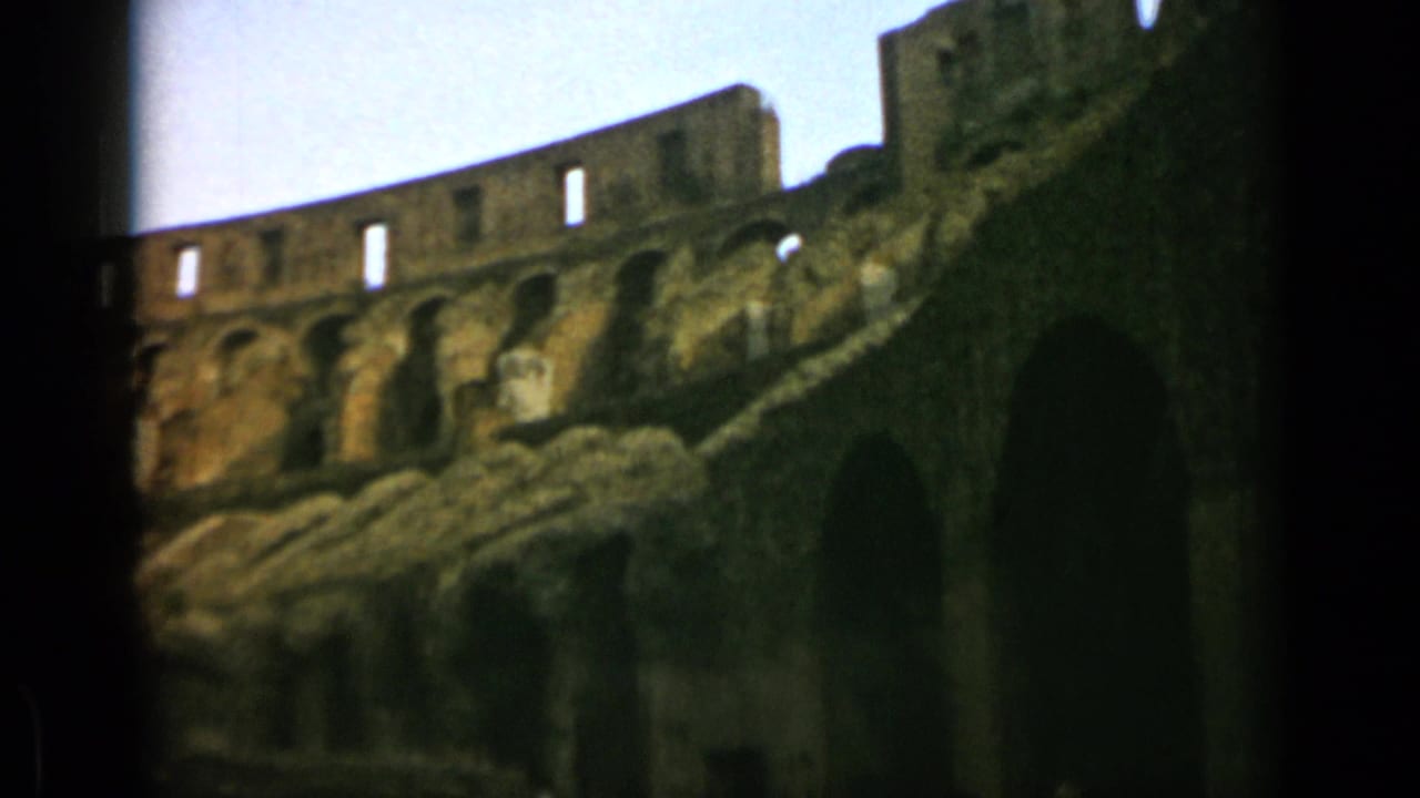 Low-angle view of the Colosseum wall with arches and stone tiers under pale sky.