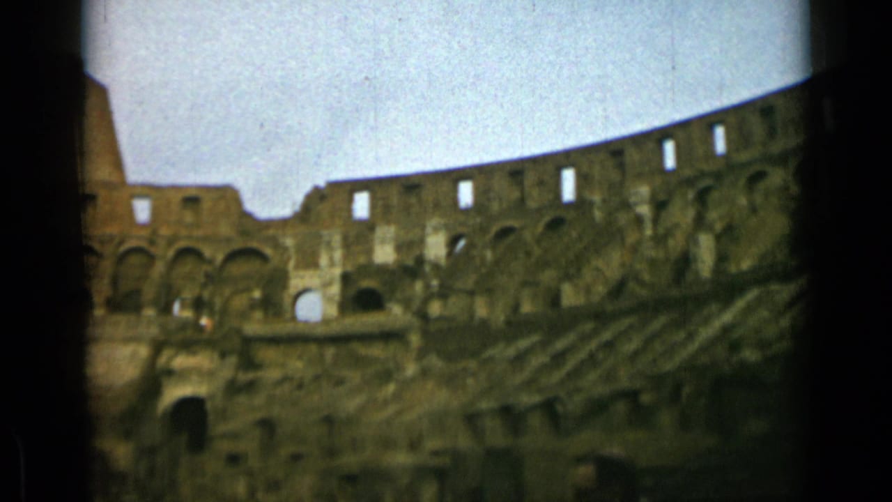 Wide view of Colosseum arches and tiered stone seating with dark film borders.