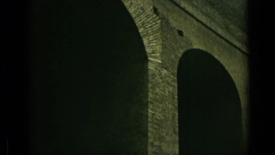 1962 Rome 8mm frame showing a close, shadowed section of a historic stone facade with tall arched openings.