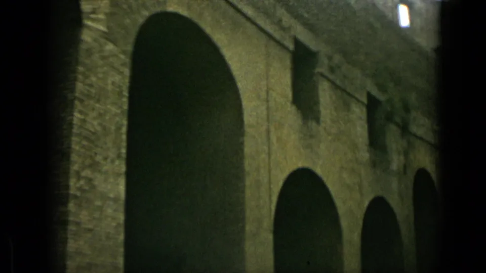 1962 Rome 8mm frame from a visitor angle, showing tall arched openings along a historic stone wall with small windows above.