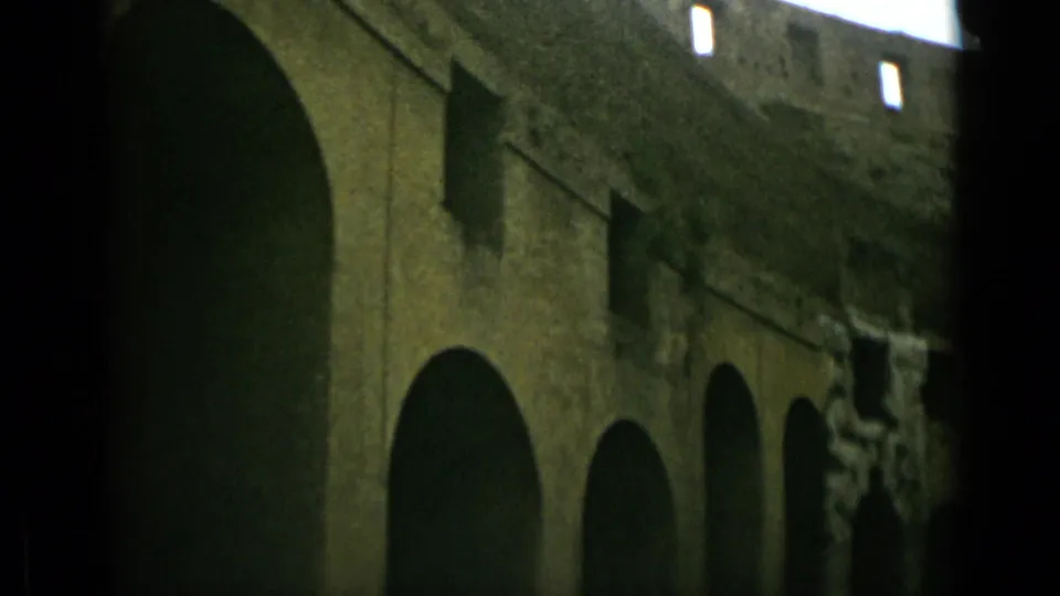 1962 Rome 8mm frame showing a longer stretch of historic stone facade with multiple arched openings and heavy shadow.