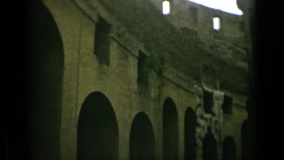 1962 home-movie frame showing shadowed Colosseum arches in Rome with rough masonry and bright openings above.