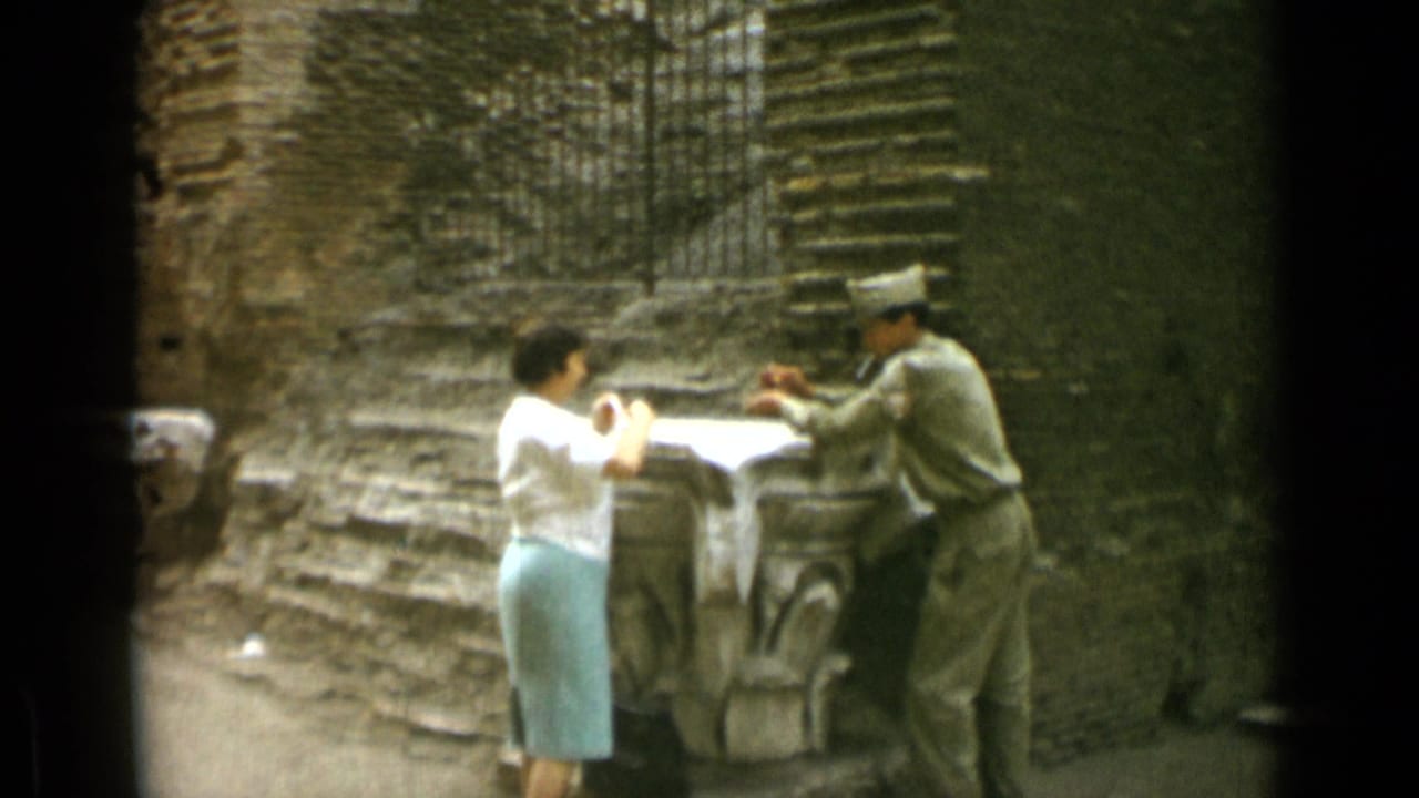 Woman and uniformed man face each other across a stone feature outdoors.