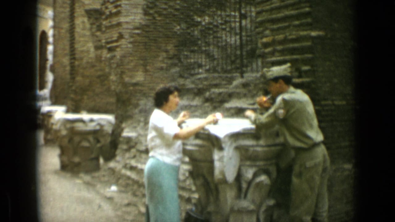 Woman and uniformed man stand at a stone table in a brick courtyard.