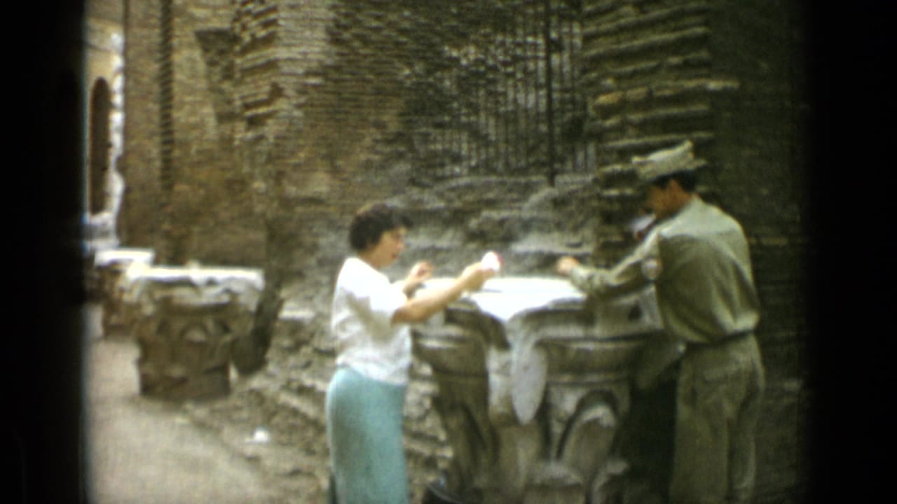 Woman and uniformed man remain beside the stone table against brick walls.