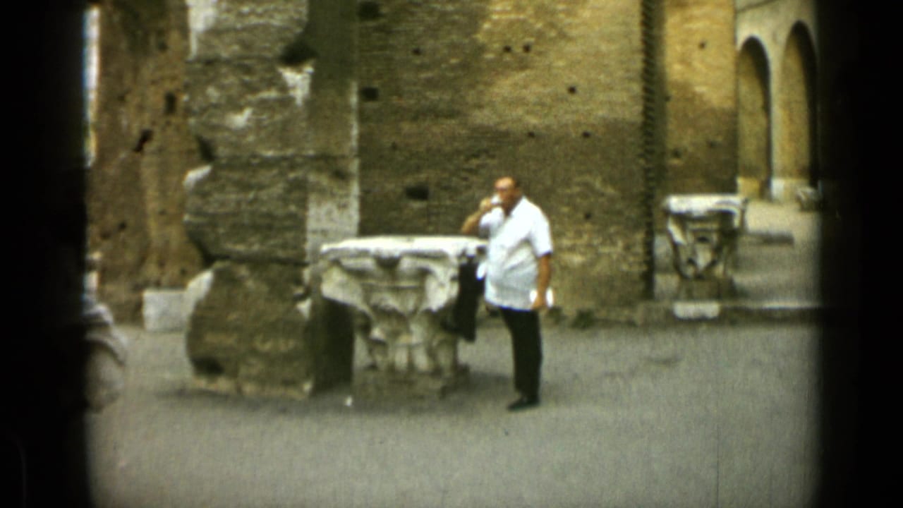 Man raises a glass beside carved stone fragments and brick walls.