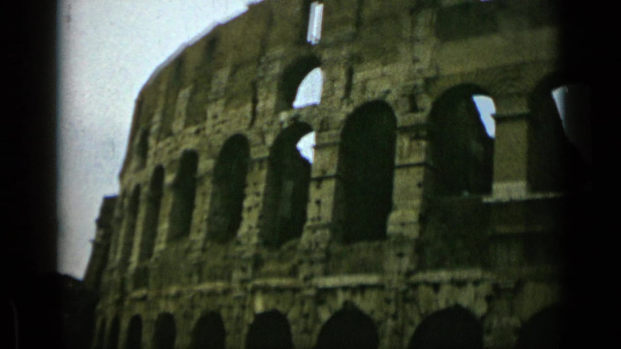1962 Rome frame showing the Colosseum exterior in soft 8mm color, with rows of arched openings and shadowed foreground edges.