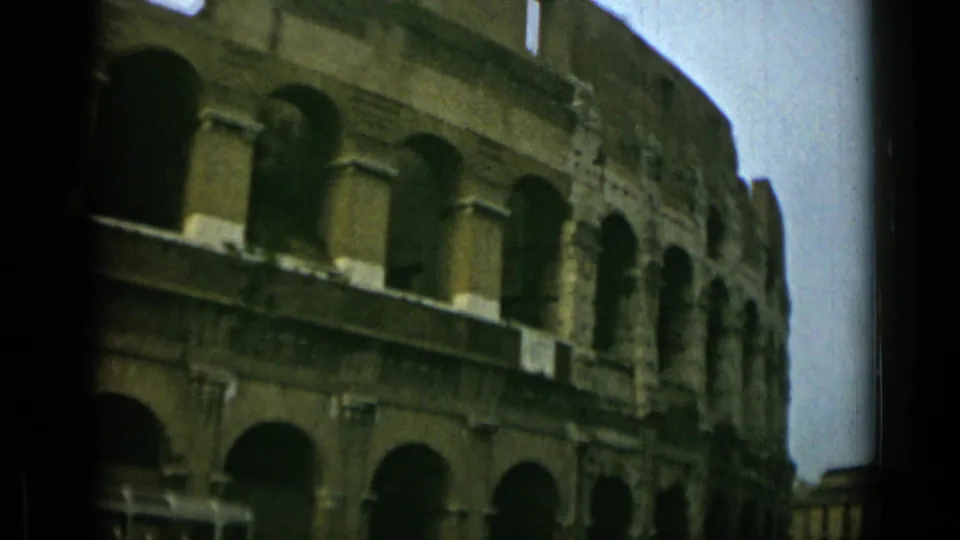 1962 visitor-shot 8mm view of the Colosseum from the street, with lower arches and a partial period vehicle at the edge.