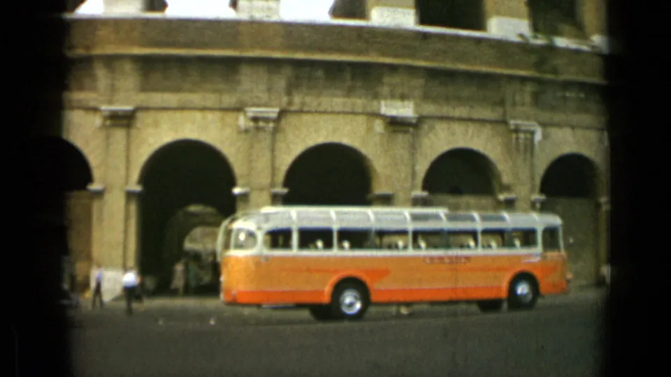 1962 Rome frame of a tour bus aligned with the Colosseum arches as pedestrians walk near the monument.