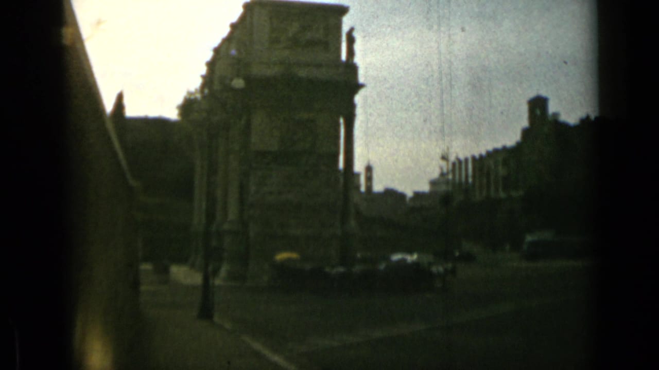 Stone archway and city street with small cars in dim 8mm frame.