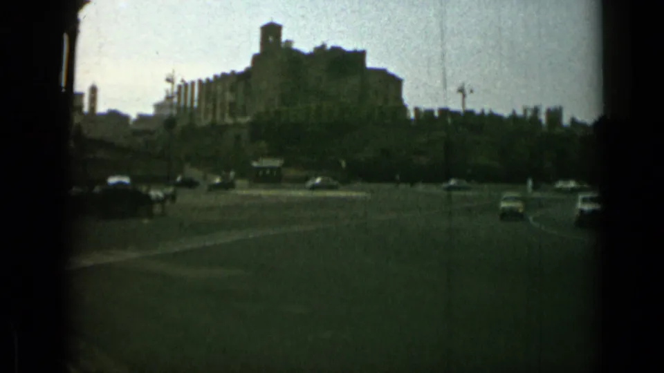 1962 Rome roadway view with period cars, a distant hilltop building, trees, and broad paved space.