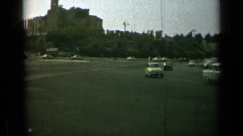 Broad 1962 Rome traffic scene with several period cars, open roadway, trees, and a large building above the road.