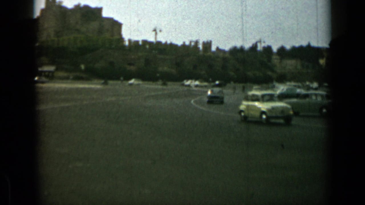 Cars moving through a broad roundabout with trees and buildings in the background.