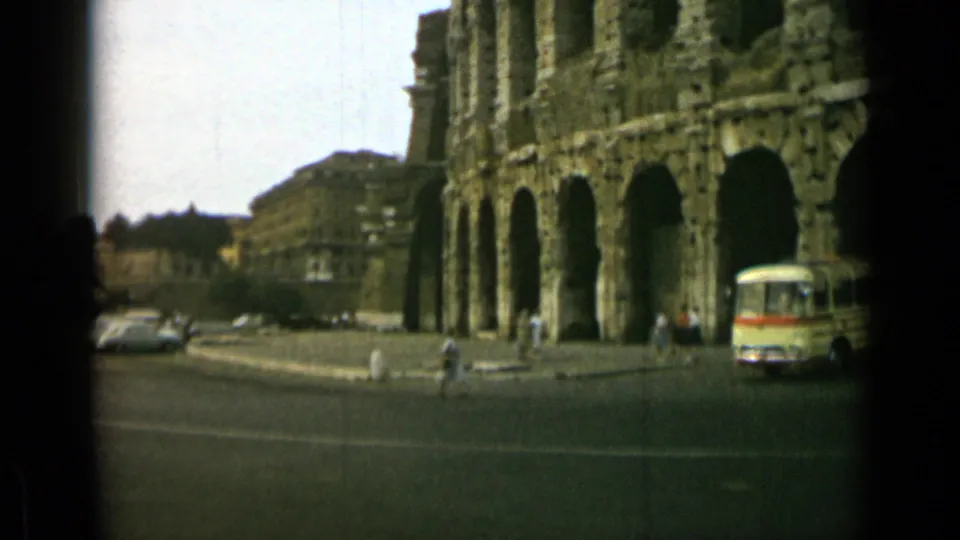 Rome street view in 1962 near a large ancient arched stone structure, with a bus, cars, and pedestrians visible.