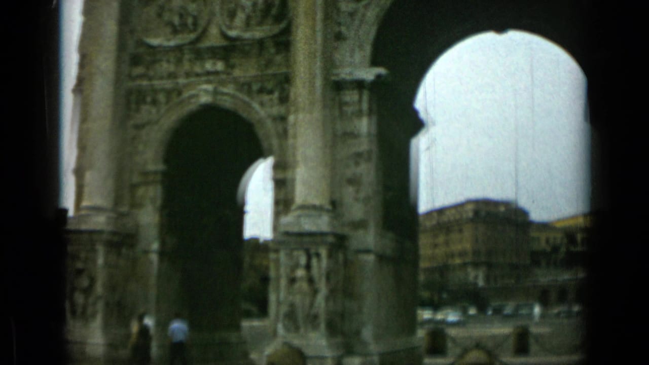 Arch of Constantine with stone arches, pedestrians, chain barriers, and Rome buildings beyond.